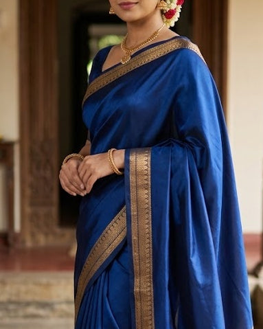 Woman in a blue saree with gold border standing in an indoor setting.