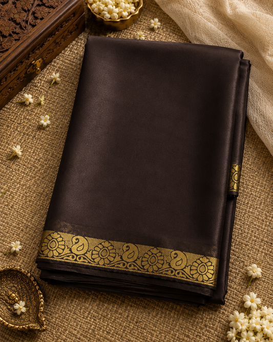 Dark brown saree with gold border on a textured surface with decorative elements.