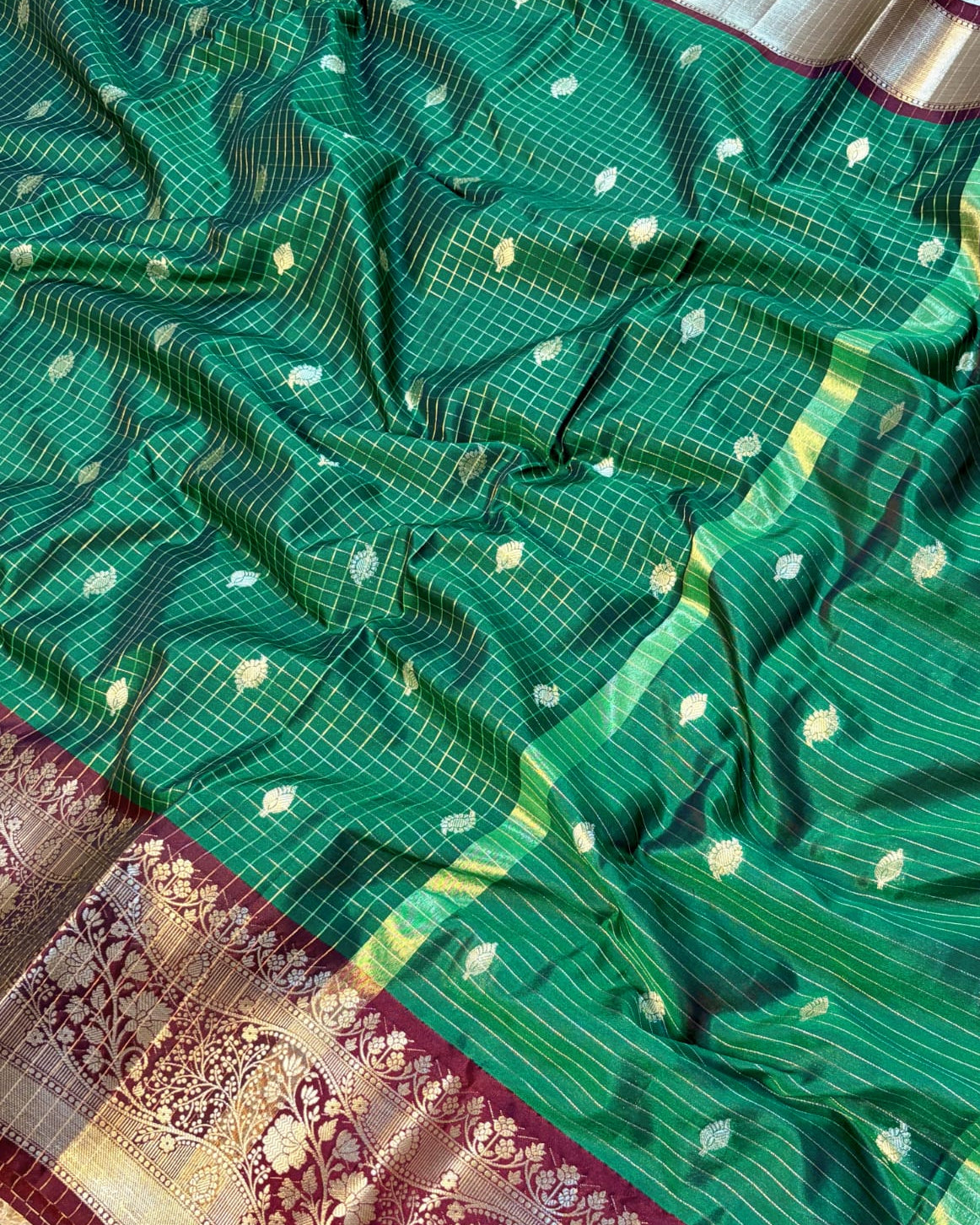 Green saree with white patterns and a maroon border on a textured surface