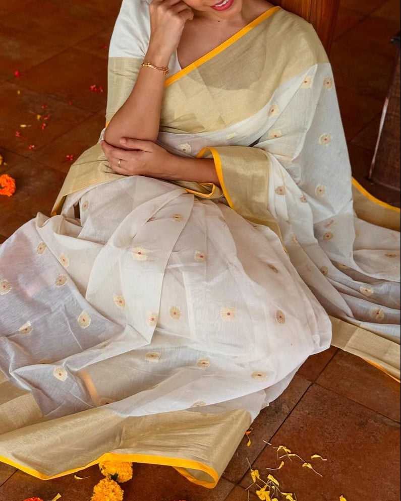 Woman in a traditional saree sitting on a wooden floor with decorative flowers around her.
