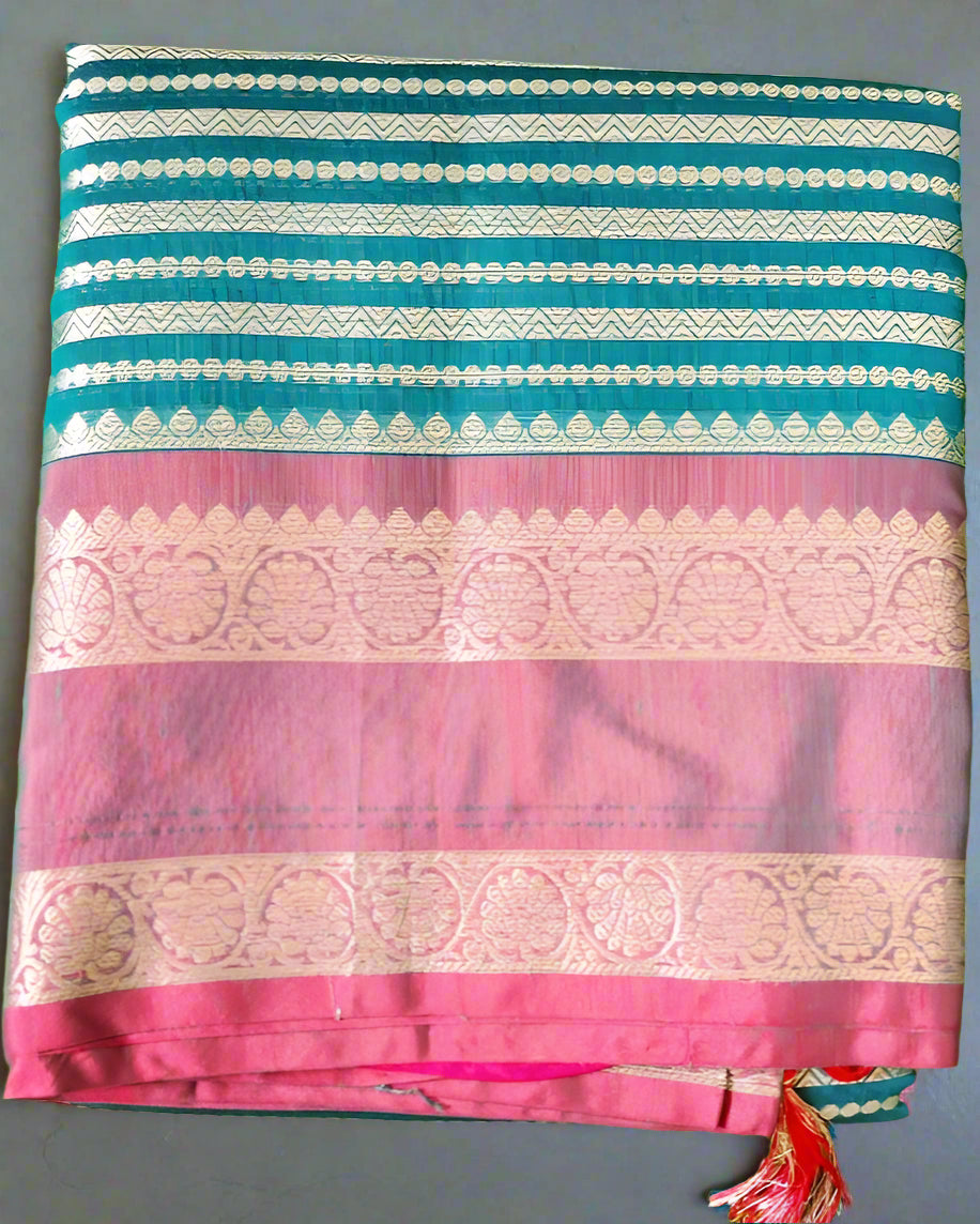 A folded Soft Litchi Silk Saree with jacquard work, displayed on a grassy surface, with a mix of green, pink, and metallic silver colors visible.