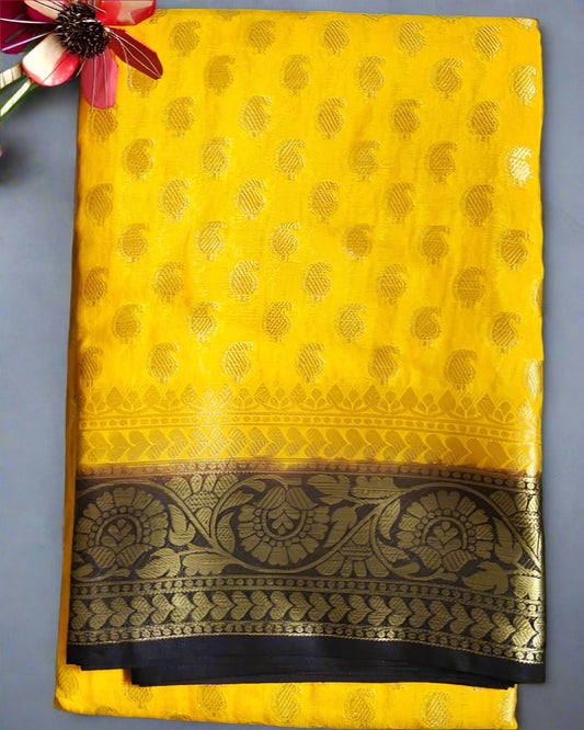 A yellow Khaddi Georgette saree with gold zari weaving displayed on a green surface, with a decorative border at the pallu.