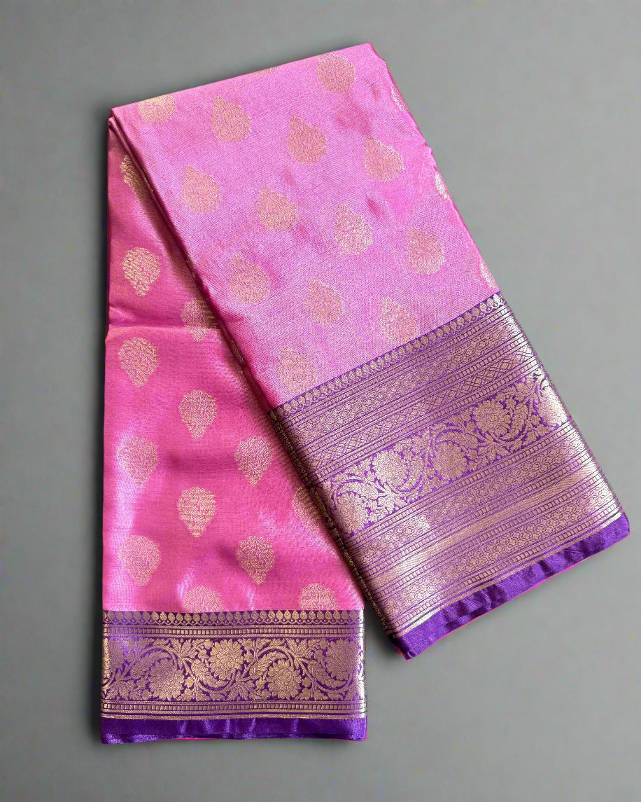 Pink saree with gold patterns and a purple border on a textured gray background