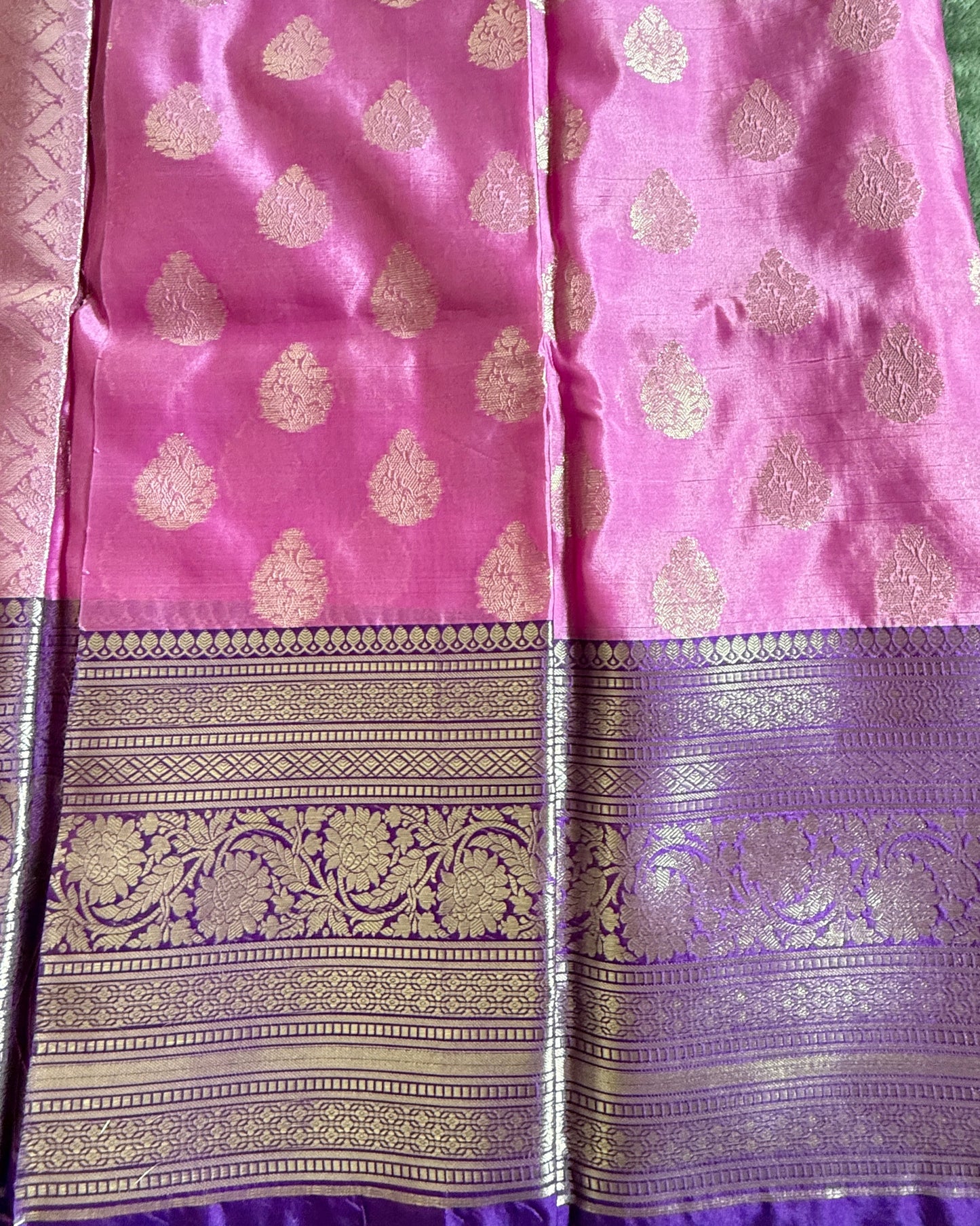 Pink and purple saree with intricate patterns on a green background