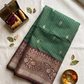 Green and brown patterned fabric on a light background with thread spools and leaves.