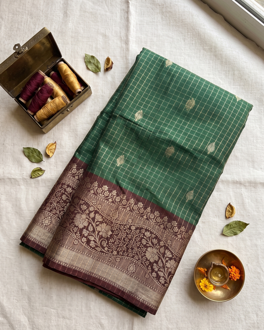 Green and brown patterned fabric on a light background with thread spools and leaves.