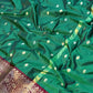 Green saree with white patterns and a maroon border on a textured surface
