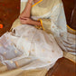 Woman in a traditional saree sitting on a wooden floor with decorative flowers around her.
