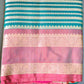 A folded Soft Litchi Silk Saree with jacquard work, displayed on a grassy surface, with a mix of green, pink, and metallic silver colors visible.