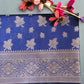 A blue saree with floral and paisley patterns displayed on a grassy surface, alongside artificial flowers.